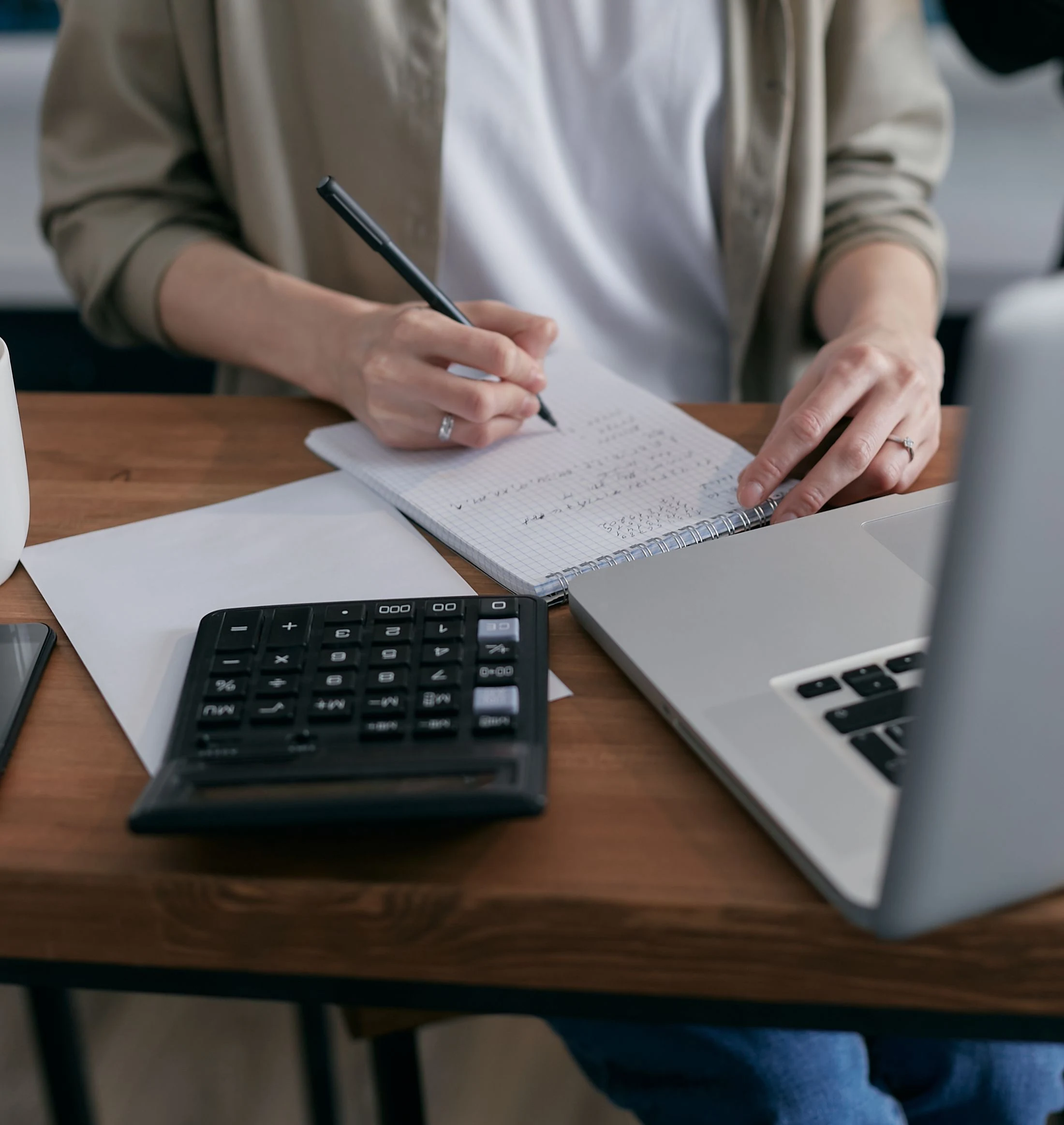 Hands reviewing notes beside a calculator and laptop